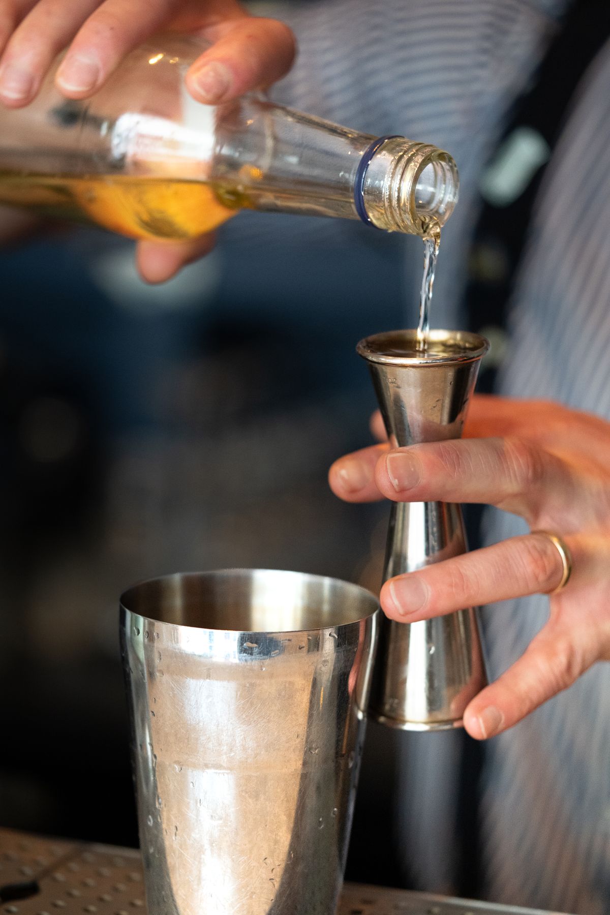 Close-up of a bartender pouring liquor into a jigger over a shaker